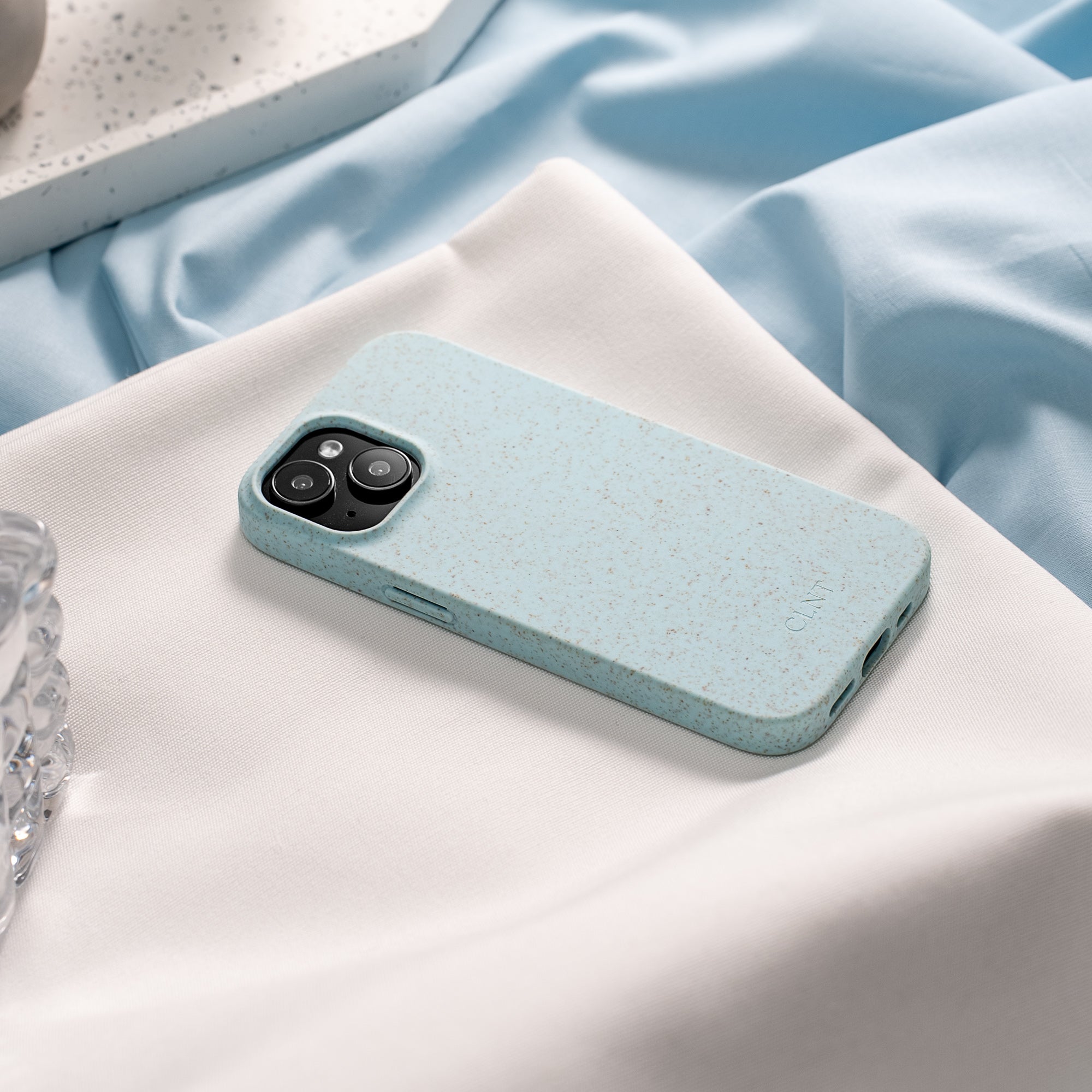 Nærbilde av lyseblått deksel til iPhone fra CLNT - vist på en lys duk hvor mobildekselet ligger på bordet.