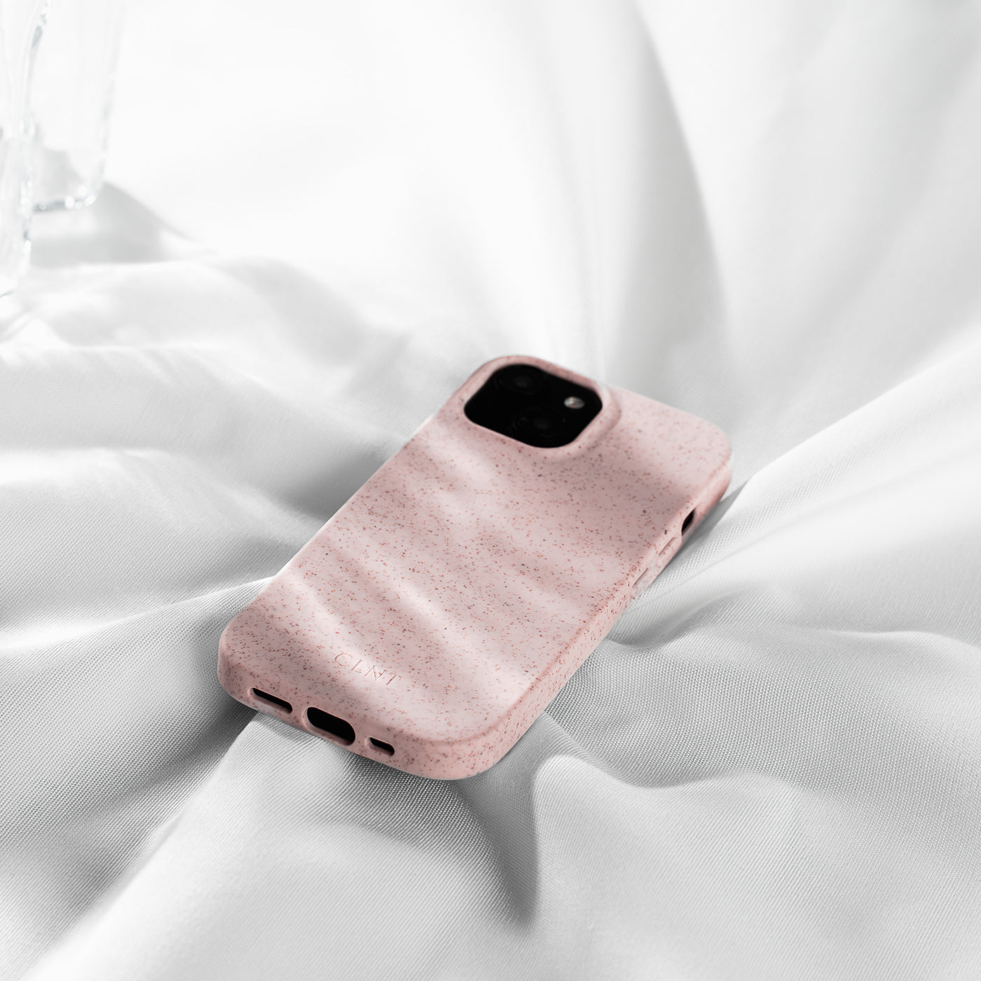 Rosa mobildeksel til iphone som ligger på en hvit dyne i sollys
