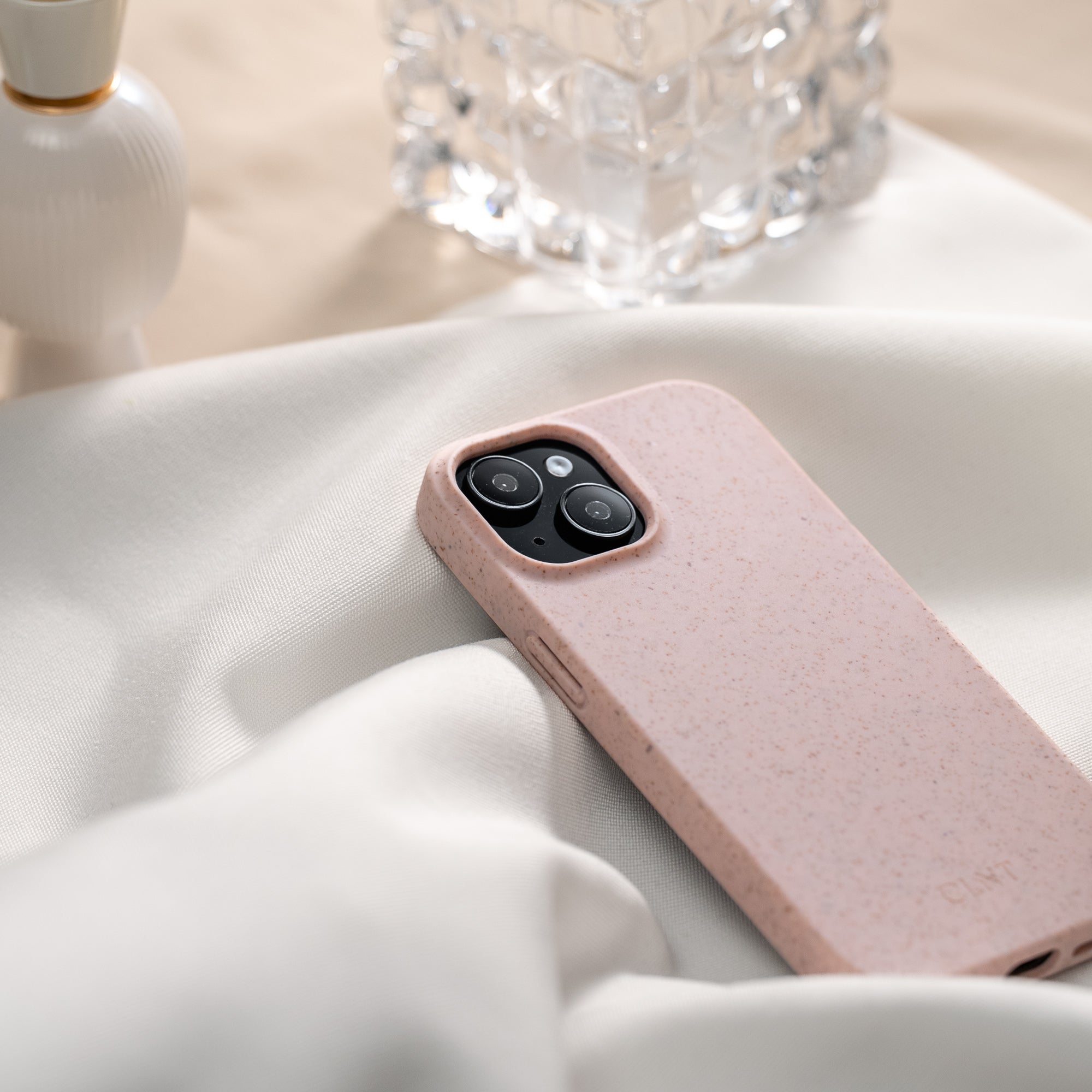 Rosa mobildeksel til iphone som ligger på en hvit duk på et silrent bord med glass og lysestaker