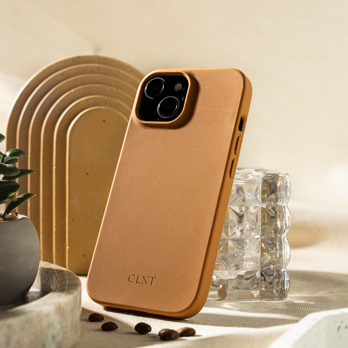 Nærbilde av rustfarget deksel til iPhone fra CLNT - vist på en lys duk hvor dekselet er stående inntil et glass.
