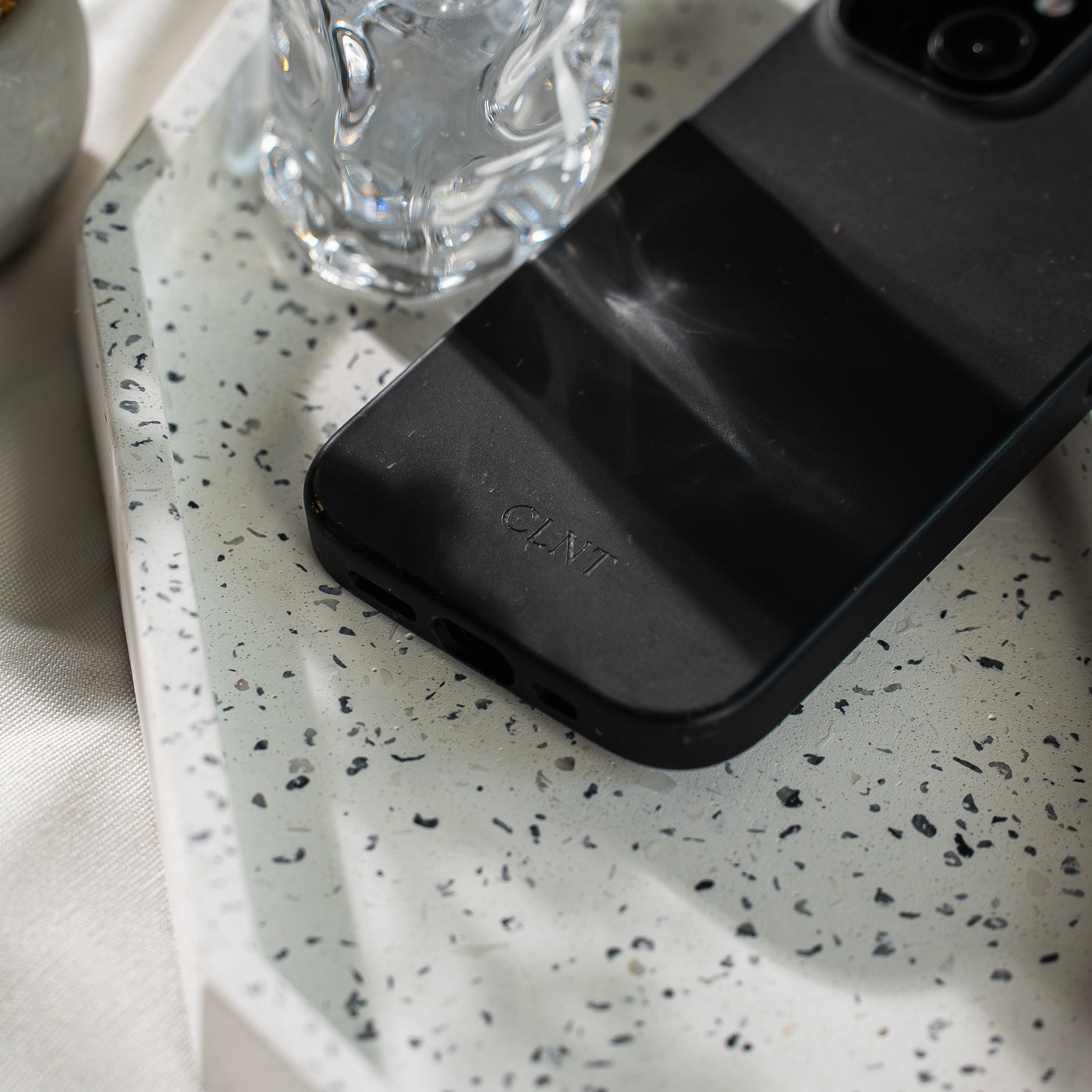 Svart iPhone-deksel fra CLNT – vist liggende på en marmorstein med sollys som danser over dekselet.