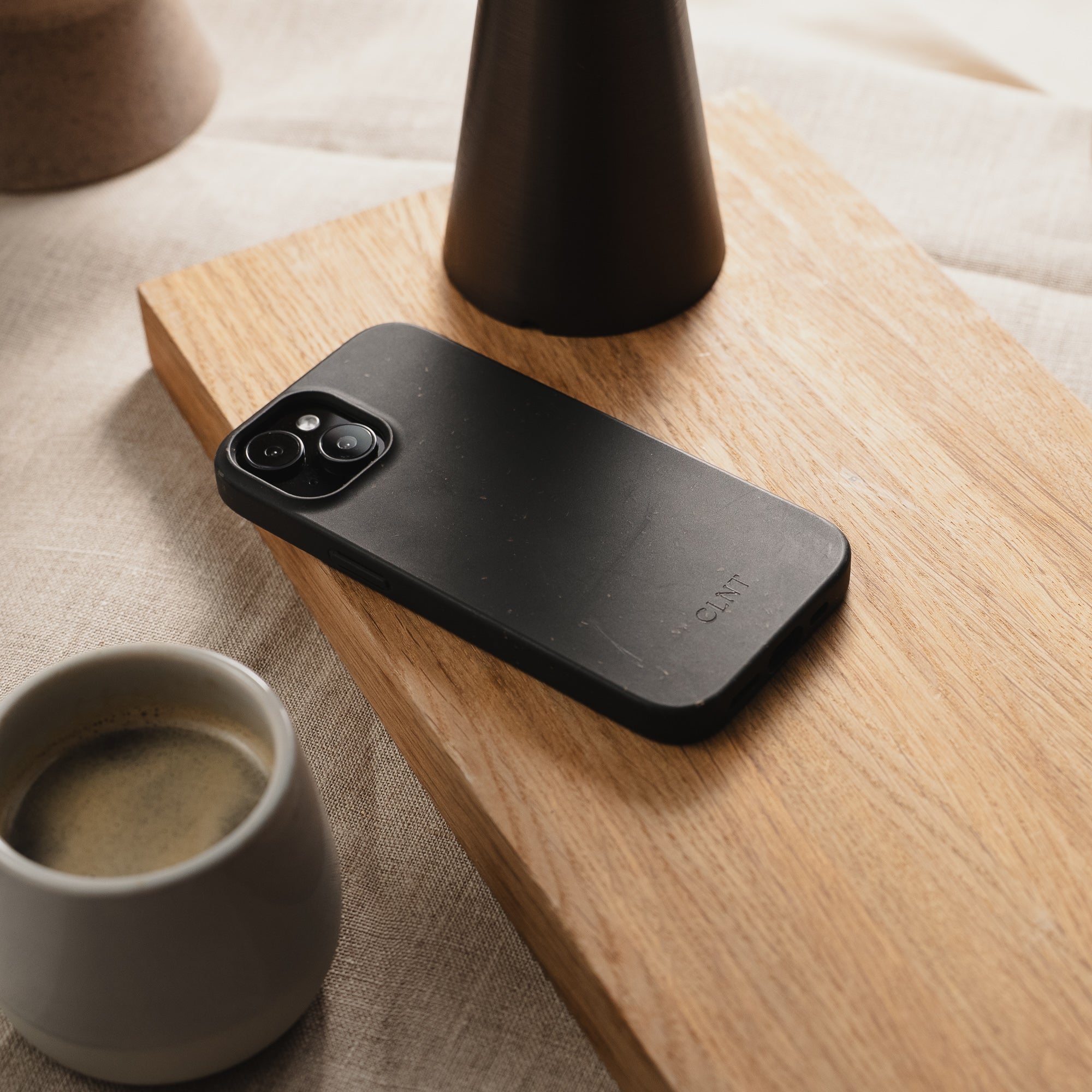 Bilde av svart deksel til iPhone fra CLNT- ligger på fjøl sammen med en kaffekopp.