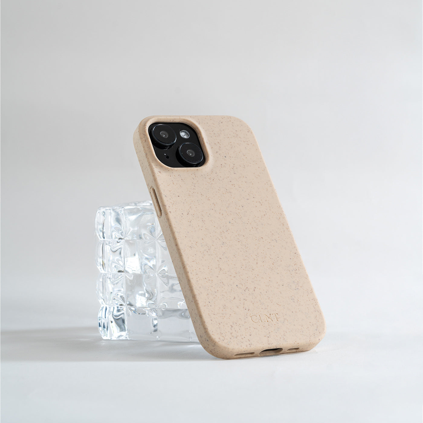 Beige iPhone deksel fra CLNT som hviler på et glass 