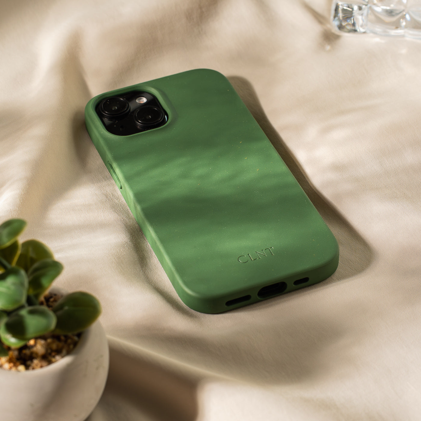Nærbilde av svart deksel til iPhone fra CLNT - vist liggende på en hvit duk med sollys over mobildekselet. 